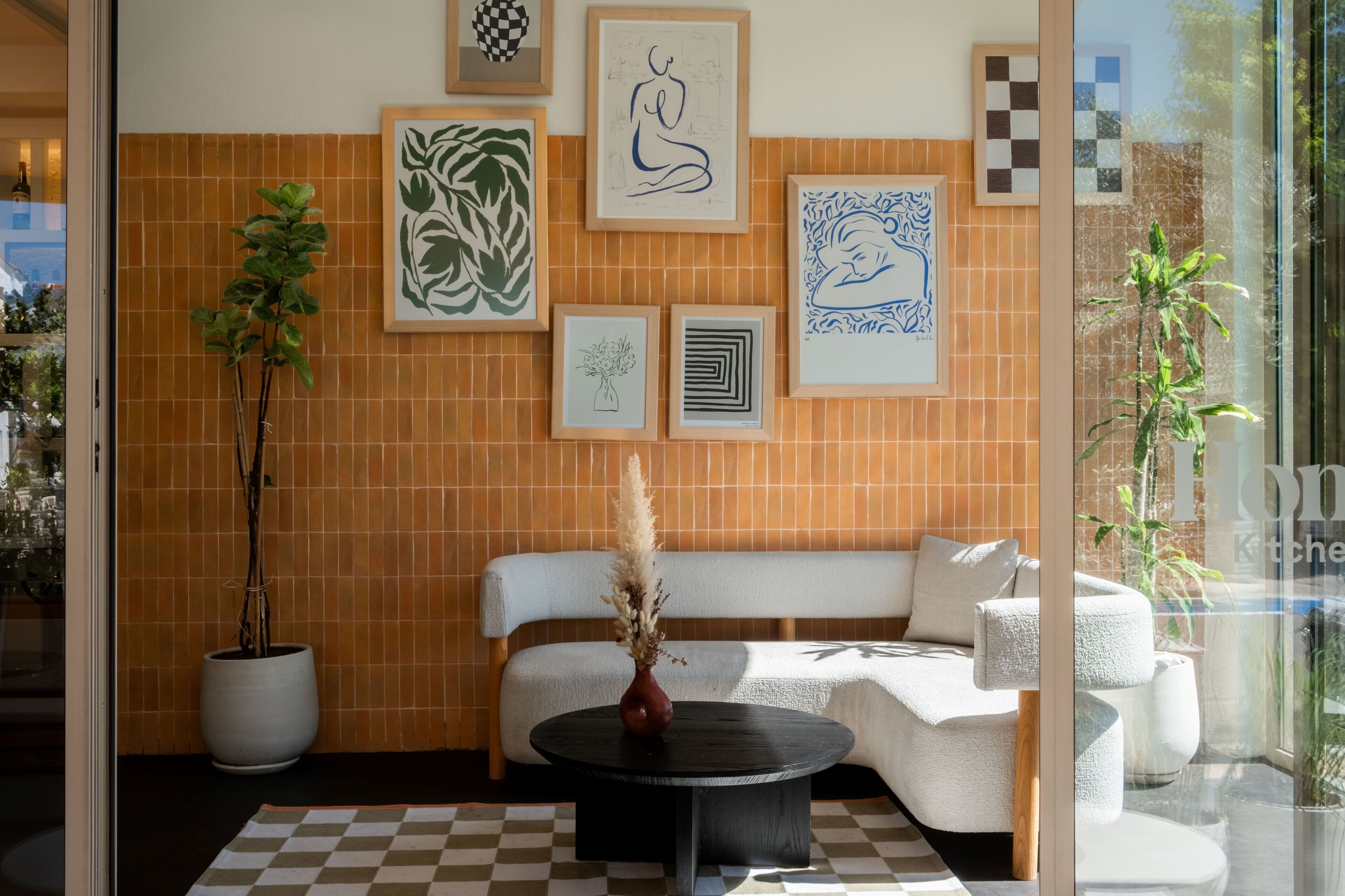 A modern interior with a white sofa, a black coffee table, and a checkered rug. There are framed artworks on the wall and a potted plant beside the sofa.