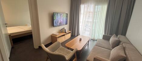 Een moderne hotelkamer met een bank, een eettafel, een televisie en een klein bureau.