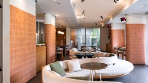 A modern lounge area with a curved white sofa, round wooden tables, and orange-tiled walls. - House of Marmaris (Marmaris)