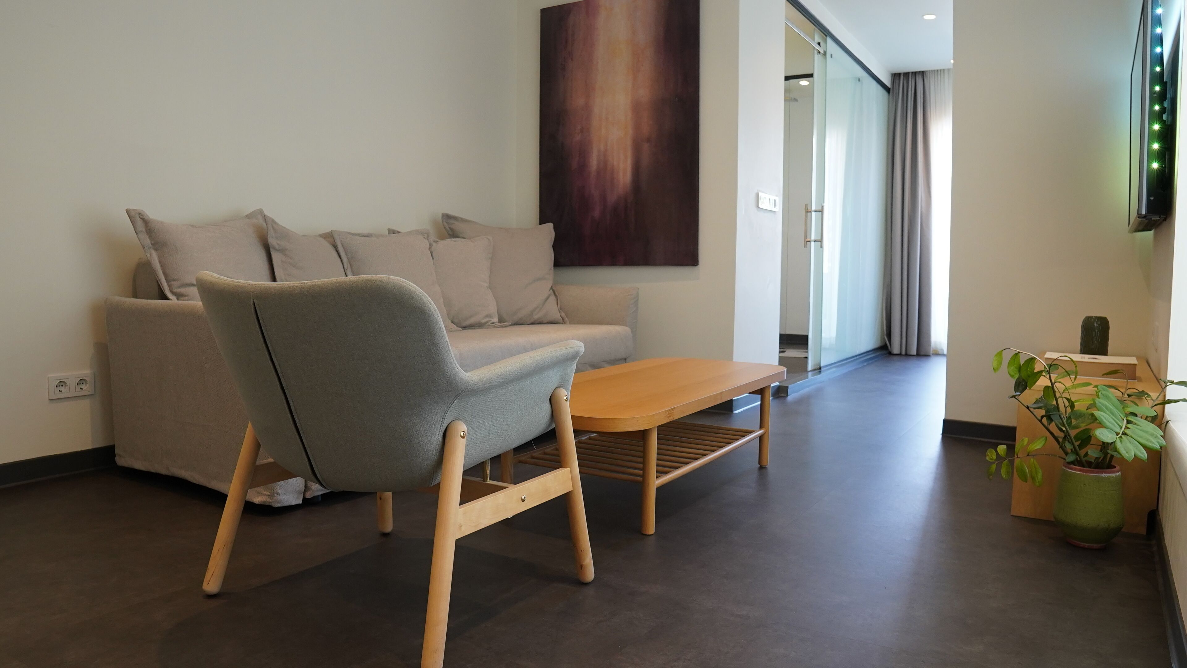 Ein modernes Wohnzimmer mit einem grauen Sofa, einem Holztisch und einem großen abstrakten Gemälde an der Wand.