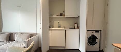 A compact living space with a bed, kitchenette, and washing machine.