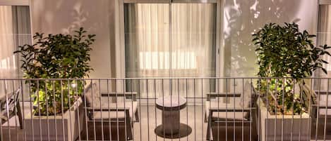 Un balcón con una mesa y dos sillas, rodeado por una barandilla de metal.