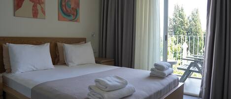 A hotel room with a large bed, a wooden headboard, and a balcony with a view of trees.