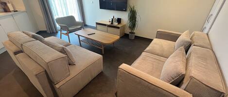 A modern living room with a sofa set, a coffee table, a TV, and a potted plant.