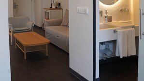 A modern hotel room with a large mirror, a sofa, a small table, and a bathroom with a bathtub and towel rack. - House of Marmaris (Marmaris)