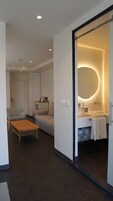 Habitación de hotel moderna con un espejo grande, un sofá, una mesita y un baño con bañera y toallero.