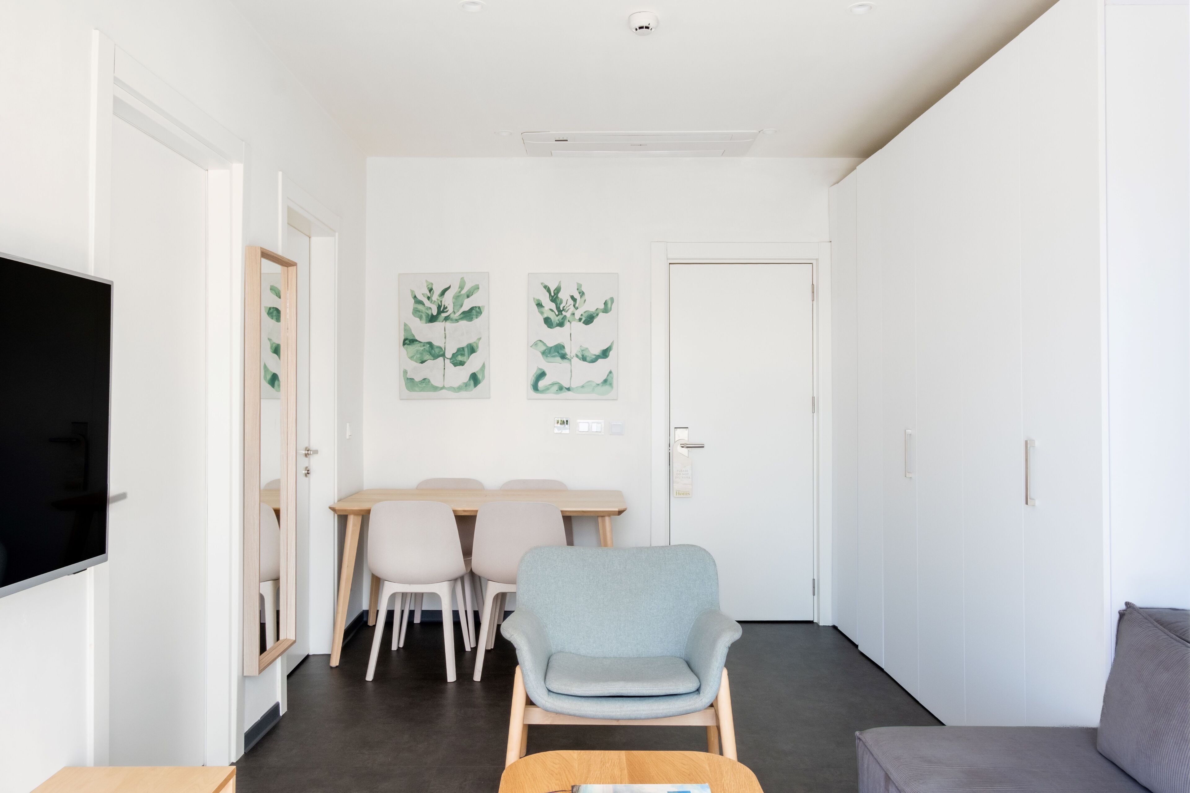 A modern living room with a flat-screen TV, a dining area with a table and chairs, and a grey armchair.