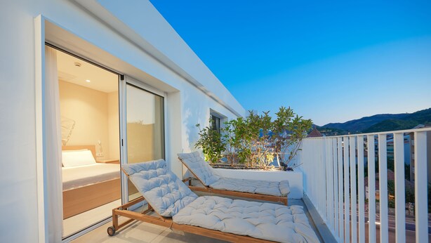 A modern balcony with two wooden beds, a sliding glass door leading to a bedroom, and a view of the cityscape. - House of Marmaris (Marmaris)