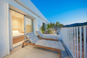 Un balcón moderno con dos camas de madera, una puerta corredera de vidrio que da a un dormitorio y vistas de la ciudad.