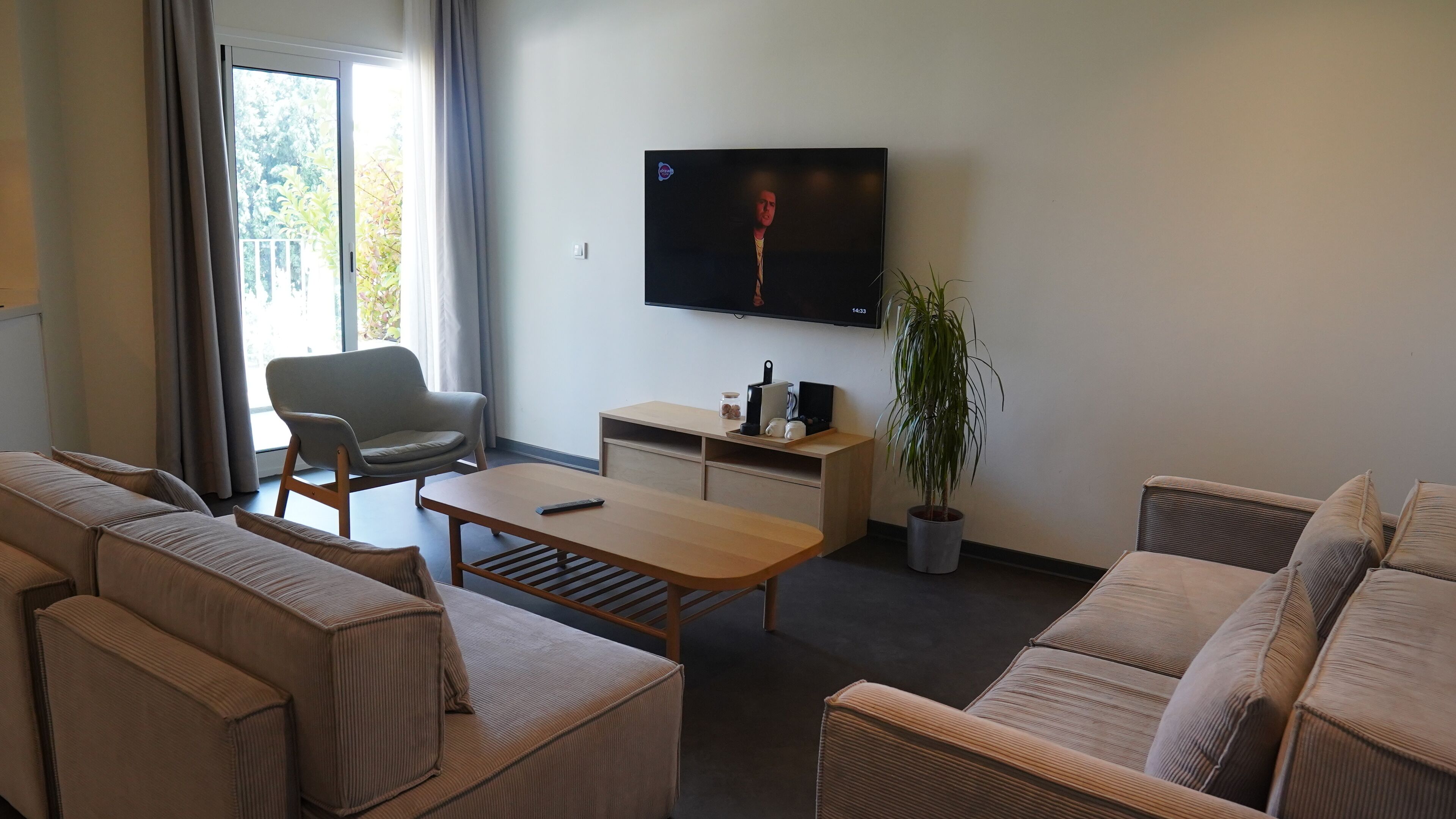 A modern living room with a sofa set, a coffee table, a TV mounted on the wall, and a potted plant.