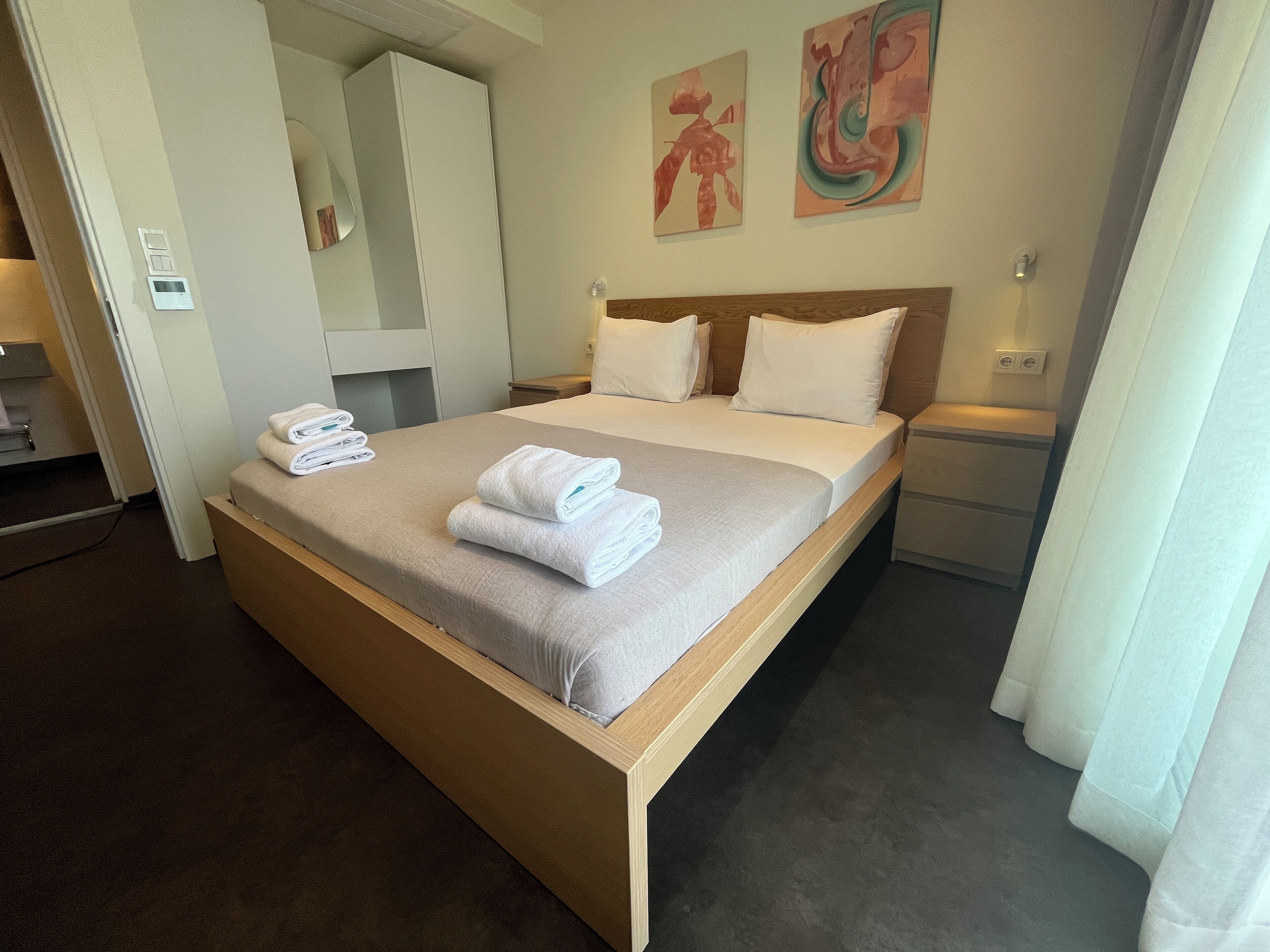 A neatly made bed with folded towels, a wooden headboard, and two wall-mounted paintings.