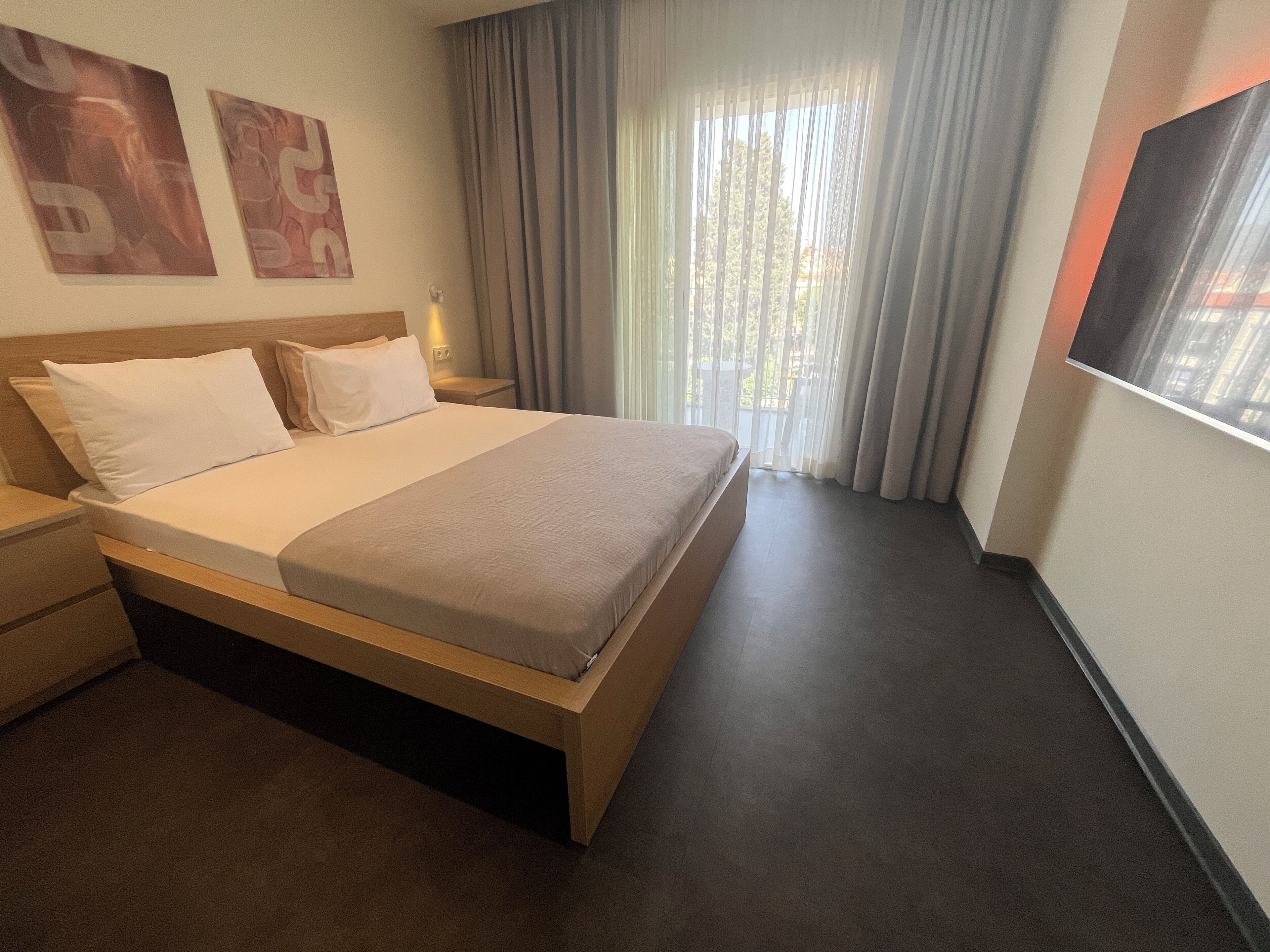 Une chambre d’hôtel avec un lit, une table de chevet, une télévision et une fenêtre avec des rideaux.