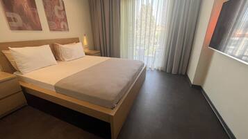 Une chambre d’hôtel avec un lit, une table de chevet, une télévision et une fenêtre avec des rideaux.