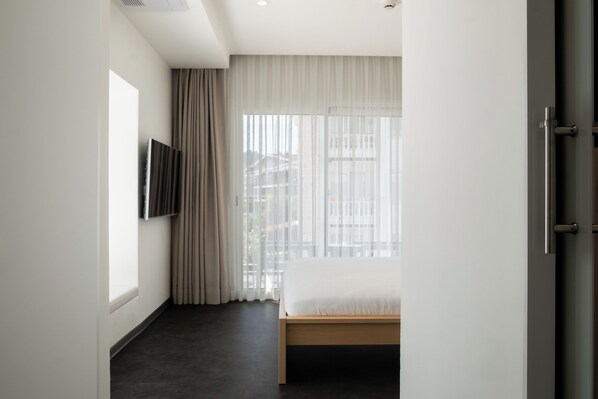 Una habitación de hotel moderna con una cama, un televisor montado en la pared y un gran ventanal con cortinas.