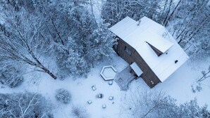 Una cabaña nevada con una terraza hexagonal y un pequeño patio.