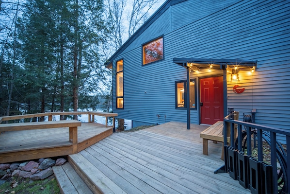 A blue wooden building with a red door, a deck, and a small outdoor seating area.
