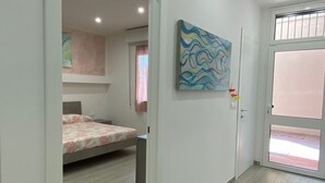 Una habitación con una cama, un cuadro en la pared y una puerta que da a otra estancia.