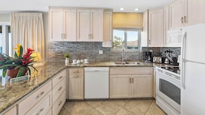 A modern kitchen with light wood cabinets, a granite countertop, a dishwasher, a stove, and a sink.