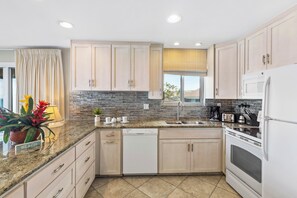 A modern kitchen with light wood cabinets, a granite countertop, a dishwasher, a stove, and a sink. - Tropical, modern finishes with vast ocean views (Lahaina)