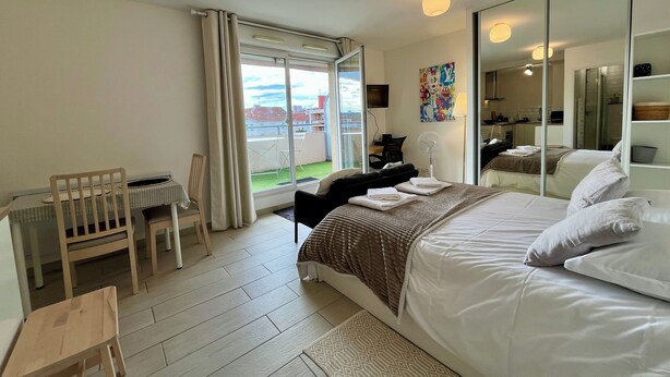 Ett hotellrum med en säng, ett skrivbord, en stol, ett fönster med gardiner, en spegel och utsikt över omgivningen.