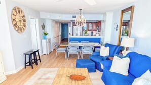 Un salon avec un canapé bleu, une table basse en bois et un coin repas avec des chaises blanches.