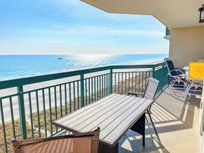 Un balcón con vista a la playa, una mesa, sillas y una lámpara de mesa amarilla.