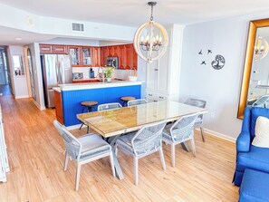Una cocina moderna con una isla central, mesa de comedor con sillas y una pared de acento azul.