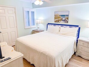 A bedroom with a bed, bedside tables, a lamp, a door, and a window with blinds.