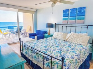 Un dormitorio con cama, mesita de noche, lámpara y vista al océano.