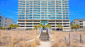 A multi-story hotel with a central entrance, surrounded by dry grass and palm trees. - North Shore Villas 806! 3BR/3BA Luxury Condo with Stunning Views! (North Myrtle Beach)
