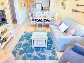 A living room with a sofa, a coffee table, and a dining area with chairs and a table. - Tilghman Beach and Racquet Club 322 (North Myrtle Beach)