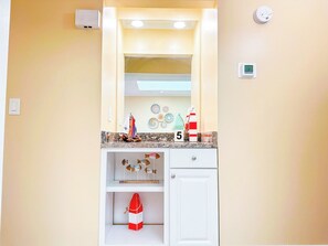 A bathroom with a vanity, a towel rack, a shelf with decorative items, and a wall-mounted heater. - Tilghman Beach and Racquet Club 322 (North Myrtle Beach)