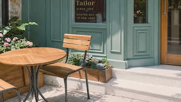 An outdoor seating area with a wooden table and bench, a potted plant, and a storefront with signage.
