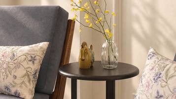 A room with a grey sofa, a small round table with a vase of yellow flowers, and a decorative horse figurine.