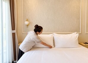 Una habitación de hotel con una cama bien hecha, una mesita de noche con un control remoto y una lámpara de pared.