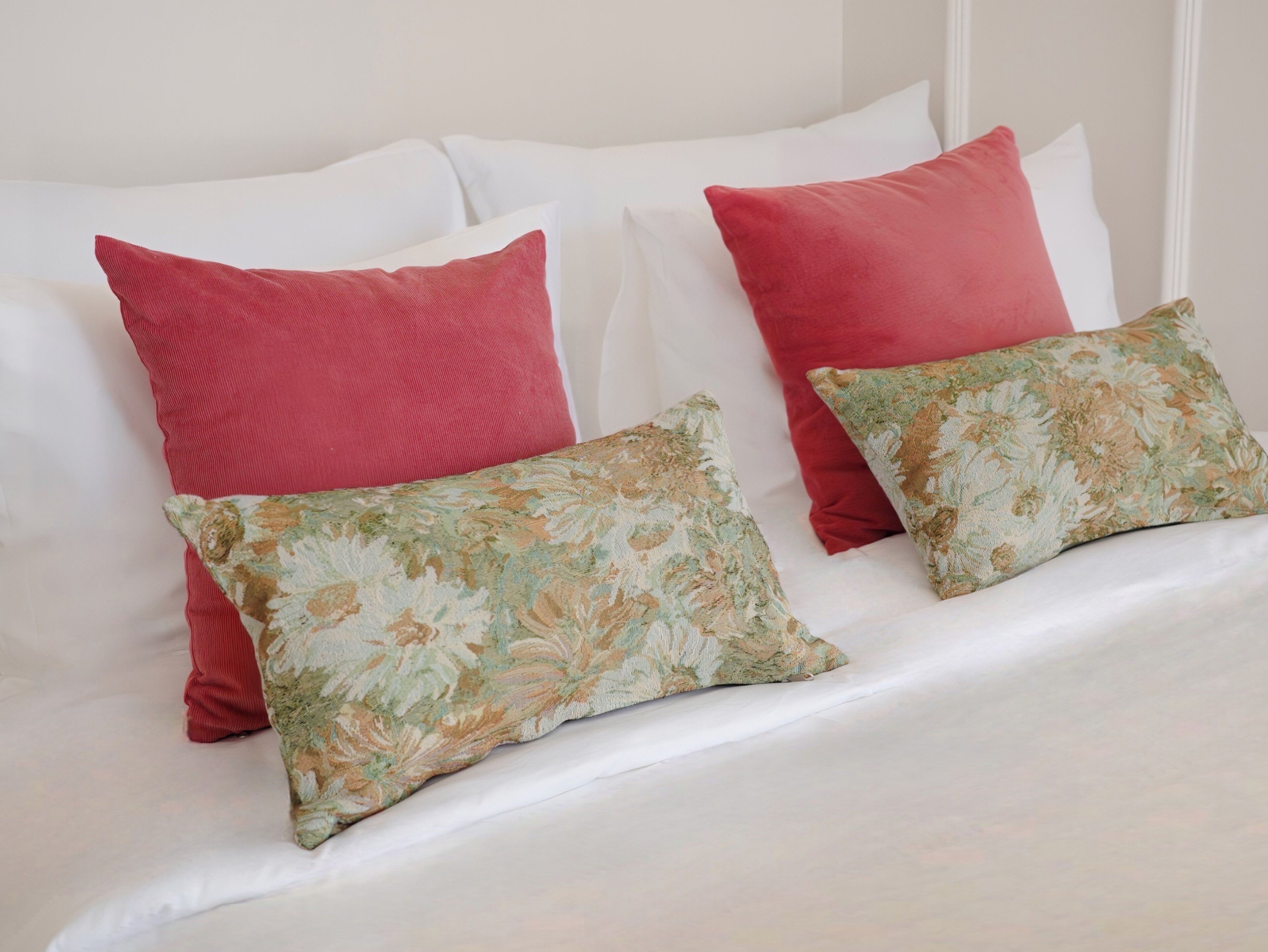 A bed with white bedding, two red pillows, and two floral-patterned pillows.