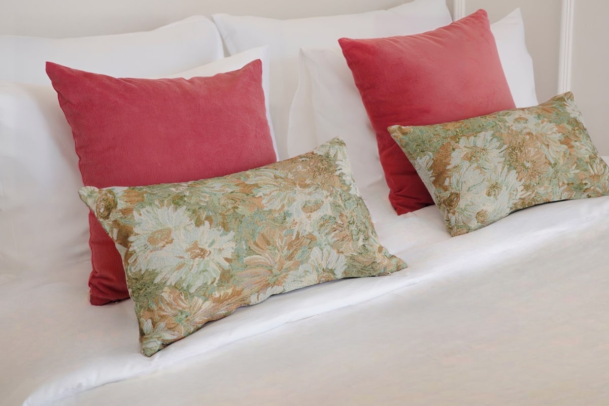 A bed with white bedding, two red pillows, and two floral-patterned pillows.
