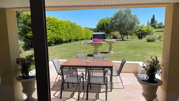 An outdoor patio with a table and chairs, surrounded by potted plants and a view of a landscaped garden. - Appartement Proche Jonzac (Meux)