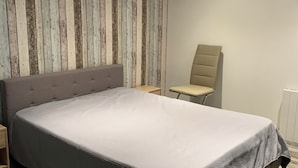 A modern bedroom with a large bed, a wooden accent wall, a chair, and a bedside table. - Appartement Proche Jonzac (Meux)