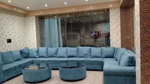 Ein modernes Wohnzimmer mit einem blauen Ecksofa, zwei Poufs und einem Glastisch.