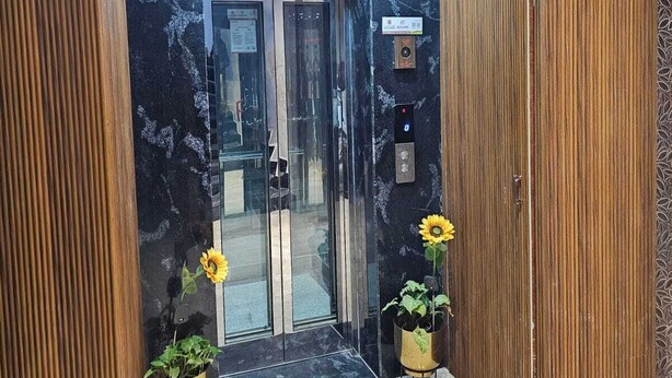 Ein Aufzug mit Marmorausstattung, Bedienfeld und zwei Ütopfpflanzen mit Sonnenblumen.