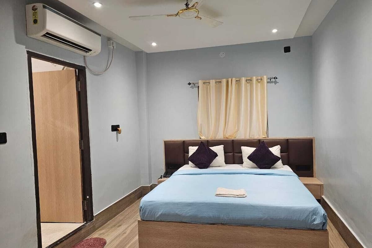 Un dormitorio con una cama, mesitas de noche, un aire acondicionado, un ventilador de techo y una puerta.
