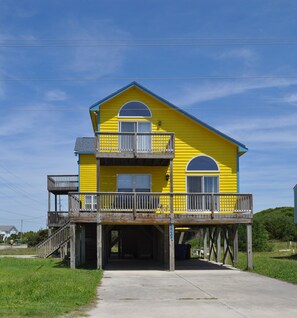 Un bâtiment jaune à deux étages, doté d’un balcon, d’une entrée couverte et d’une terrasse en bois.