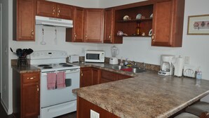 A kitchen with wooden cabinets, a white stove, a microwave, a toaster, and a coffee maker. - Finisterre – Your Topsail Island Escape (North Topsail Beach)