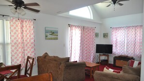 A living room with two sofas, a TV, a ceiling fan, and a painting on the wall. - Finisterre – Your Topsail Island Escape (North Topsail Beach)