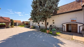 Ein Wohnhaus mit gepflasterter Auffahrt, einem großen immergrünen Baum und einem Gebäude mit einem Ziegeldach und einer kleinen Terrasse.