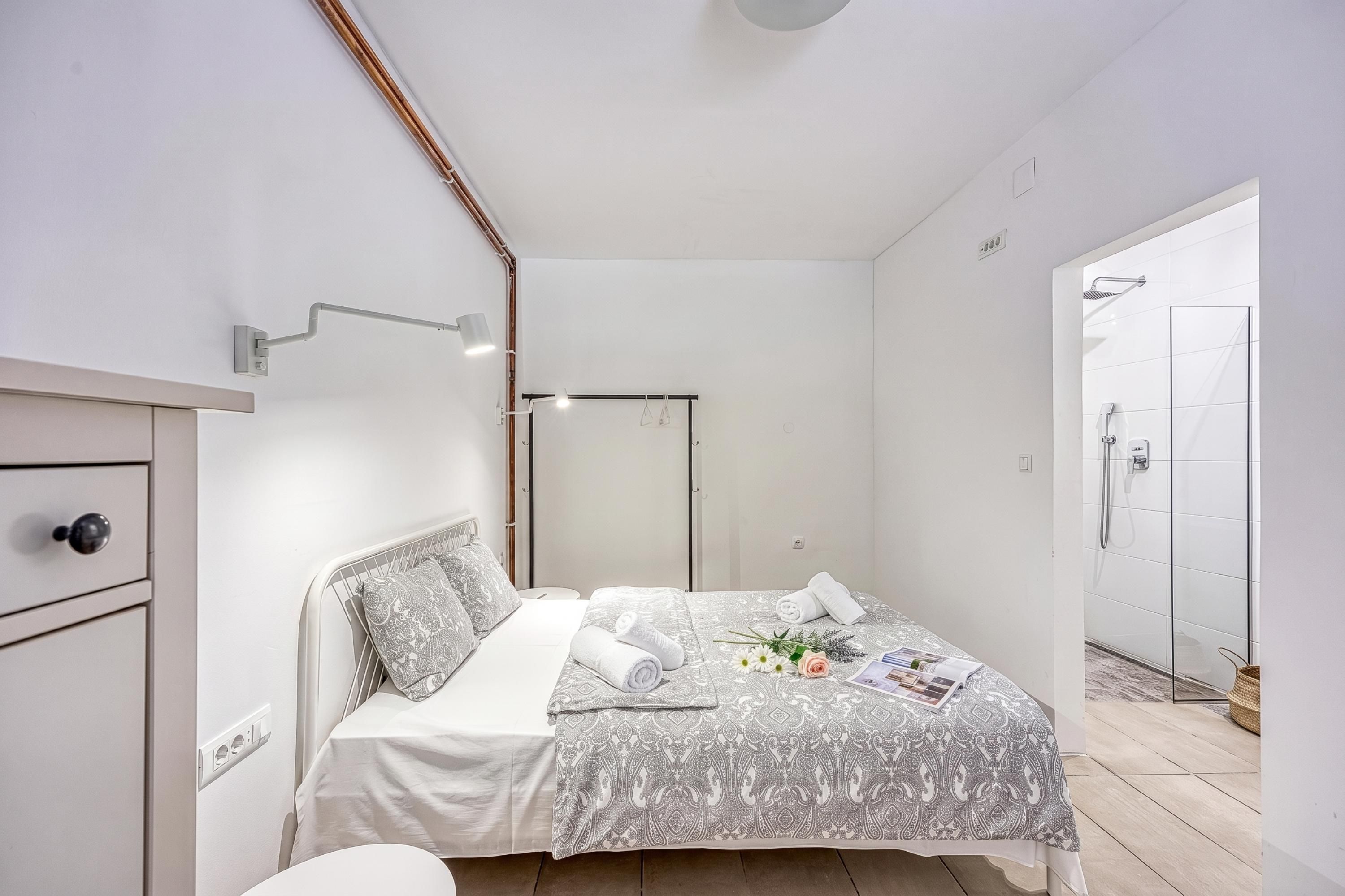 A modern bedroom with a bed, bedside table, and a shower area.