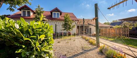 A residential area with a house featuring a red roof, a gravel pathway, and a variety of plants and flowers.