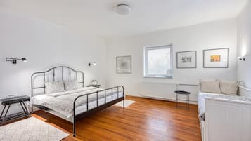 Ein Schlafzimmer mit Bett, Nachttischen, einem Heizkörper, einem Fenster mit Jalousien und Wandbildern.