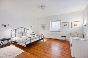 Un dormitorio con cama, mesitas de noche, radiador, ventana con persianas y una obra de arte en la pared.